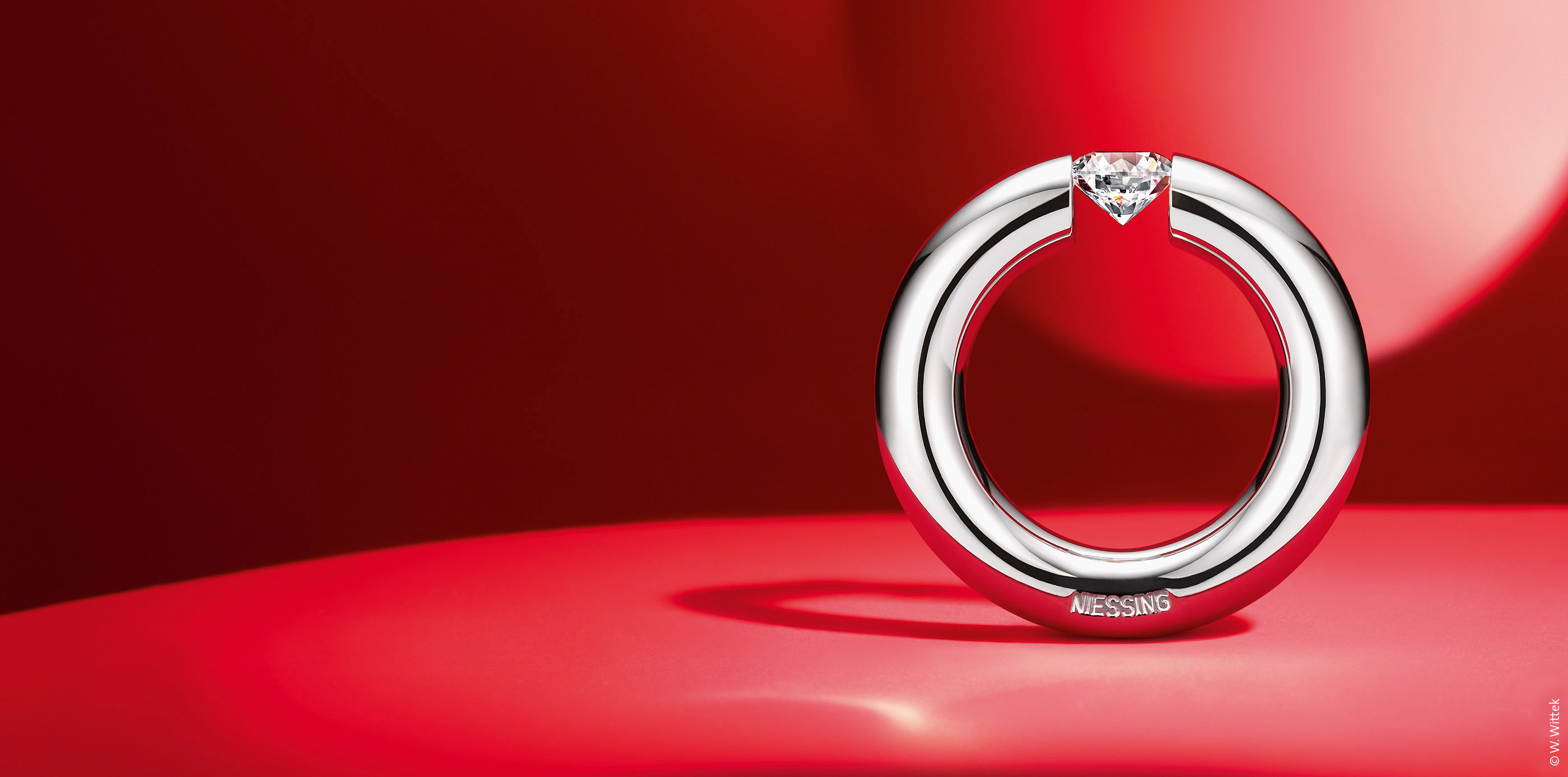 Runder Ring mit eingefasstem Stein auf rotem Hintergrund